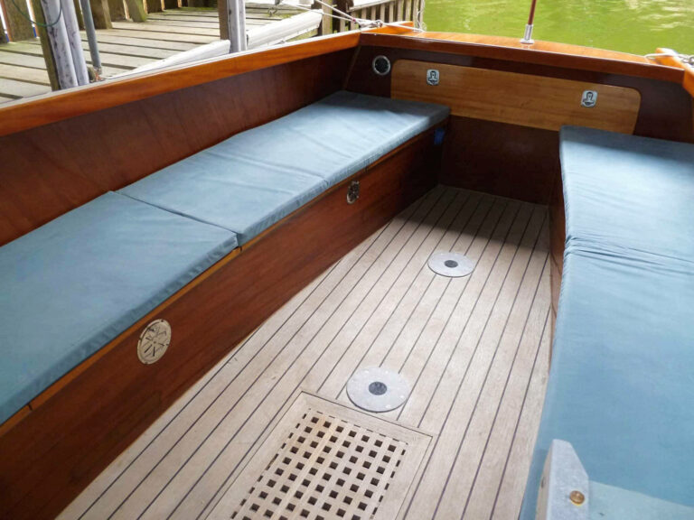 Aft cockpit of Frog Prince with blue cushioned bench seating and varnished wood finish.