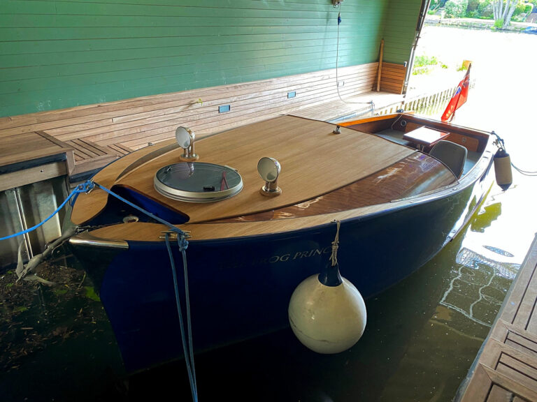 Bow view of electric launch Frog Prince, showing cedar deck, chrome vents, and Union Jack flag.
