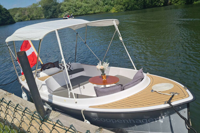 Scoopenhagen electric launch with canopy, table, and cushions arranged for river leisure.