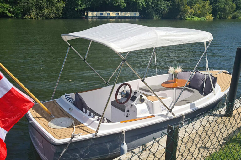 Stern and helm view of Scoopenhagen, Ruban Bleu Scoop+, moored on the Thames with canopy and Danish flag.