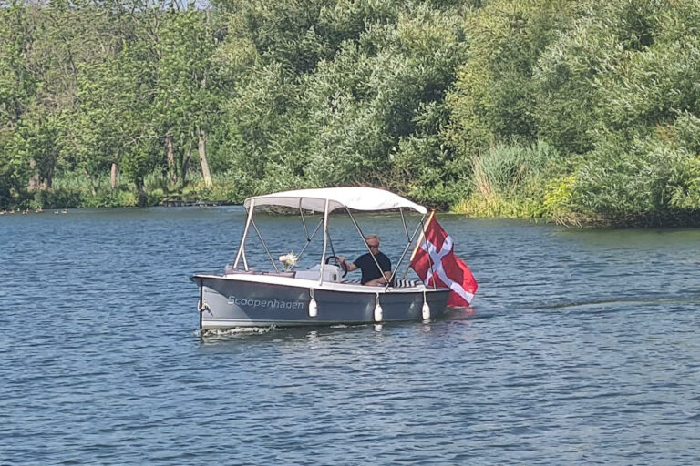 Scoopenhagen electric boat cruising on the river, canopy raised and Danish flag flying.