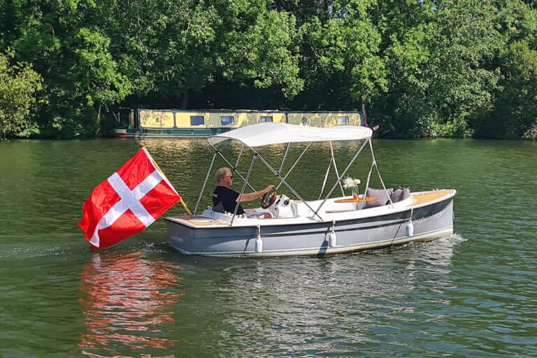 Scoopenhagen quarter view on the river, helm position aft, canopy raised, grey hull.