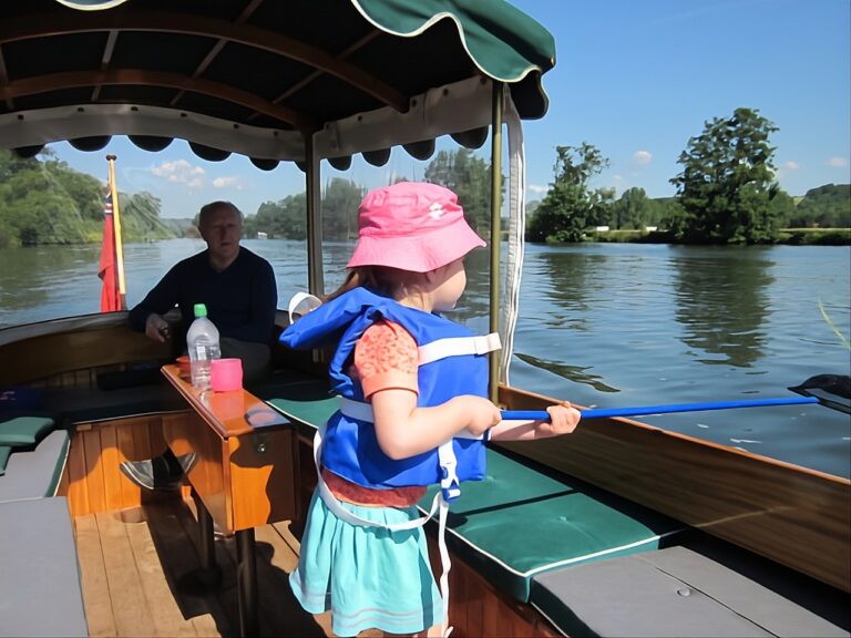 Interior of Frolic 21 electric boat showing mahogany seating, green cushions and family cruising on the Thames